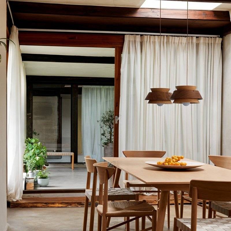 Two Clérachic layered wood pendants in oak and walnut hung over a pale wood dining table with woven-seat chairs.