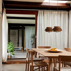 Two Clérachic layered wood pendants in oak and walnut hung over a pale wood dining table with woven-seat chairs.