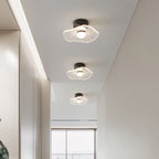 Three ribbed acrylic ceiling lights step down a white corridor towards a bright window, a Clérachic ceiling light.