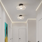 Two lit ceiling lights with wavy shades in a hallway edged with a strip of warm light, from Clérachic.