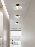 Three wavy acrylic ceiling lights in a row along a white hallway to a bright window, a Clérachic ceiling light.