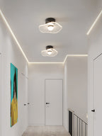 Two ceiling lights with ribbed shades along a white hallway lit with a perimeter glow, a teal artwork on the wall, from Clérachic.
