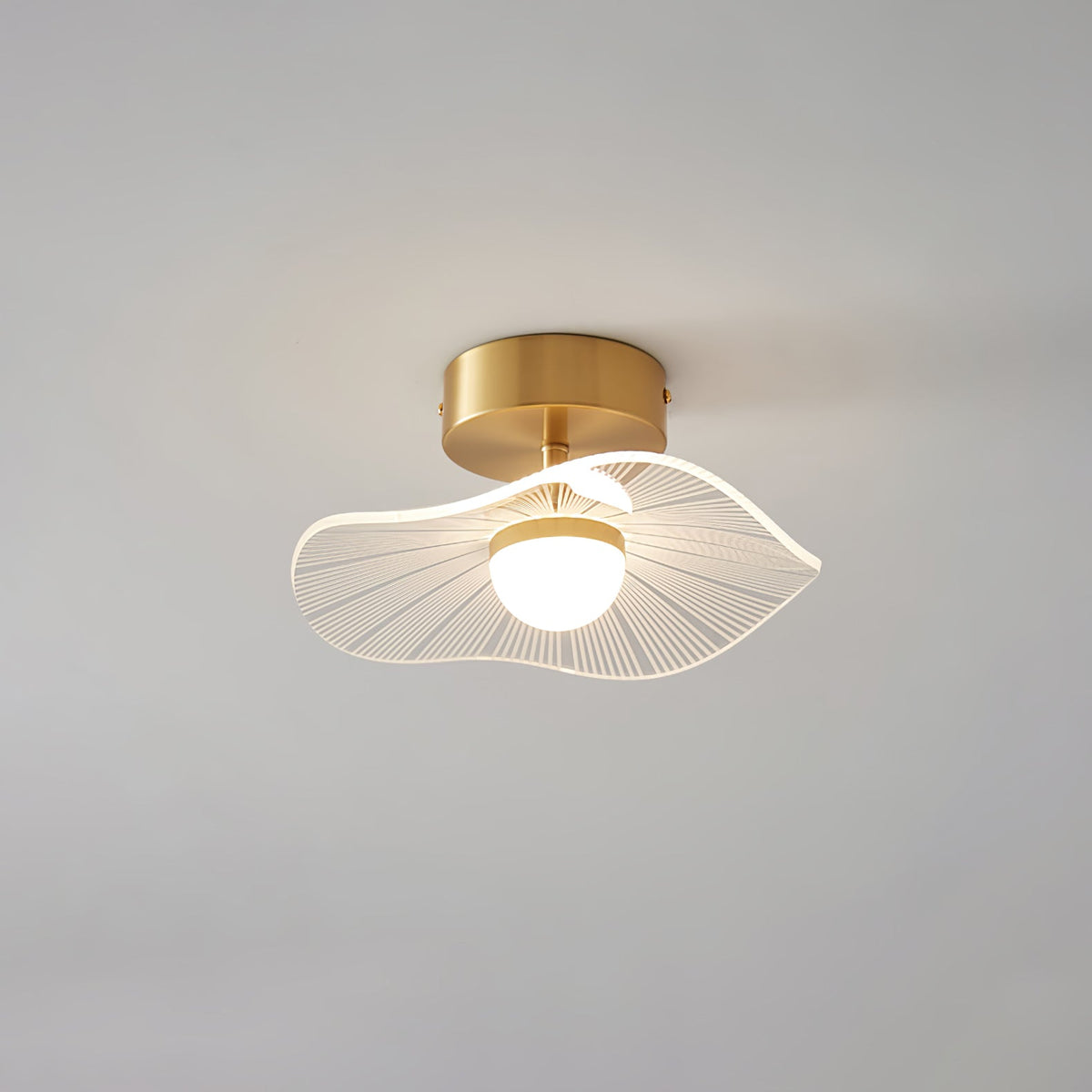 Brass ceiling light with a wavy ribbed shade and lit globe, hanging close to a grey ceiling, from Clérachic.