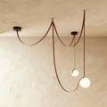 Clérachic leather and glass chandelier with two frosted glass globes on russet leather straps, unlit against a plaster ceiling.