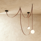 Clérachic leather and glass chandelier with two frosted glass globes on russet leather straps, unlit against a plaster ceiling.