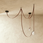 Clérachic pendant chandelier showing two glass globe shades on looping leather straps, unlit against a warm plaster ceiling.