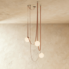 Clérachic leather and glass chandelier with three frosted glass globes cascading on tan leather straps against a plaster ceiling.