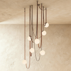 Clérachic leather and glass chandelier with seven frosted glass globes cascading on russet leather straps against a plaster ceiling.