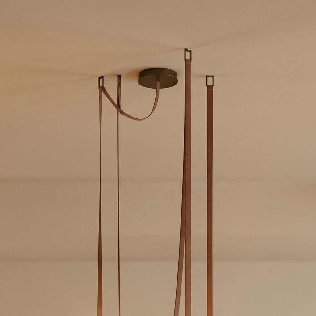 Close-up of a Clérachic chandelier's leather straps and brass ceiling canopy, showing the cord and mounting detail.