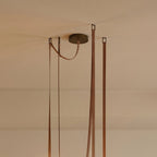 Close-up of a Clérachic chandelier's leather straps and brass ceiling canopy, showing the cord and mounting detail.
