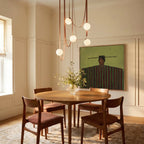 A lit Clérachic chandelier with five glass globes cascades on leather straps above a round wood dining table.