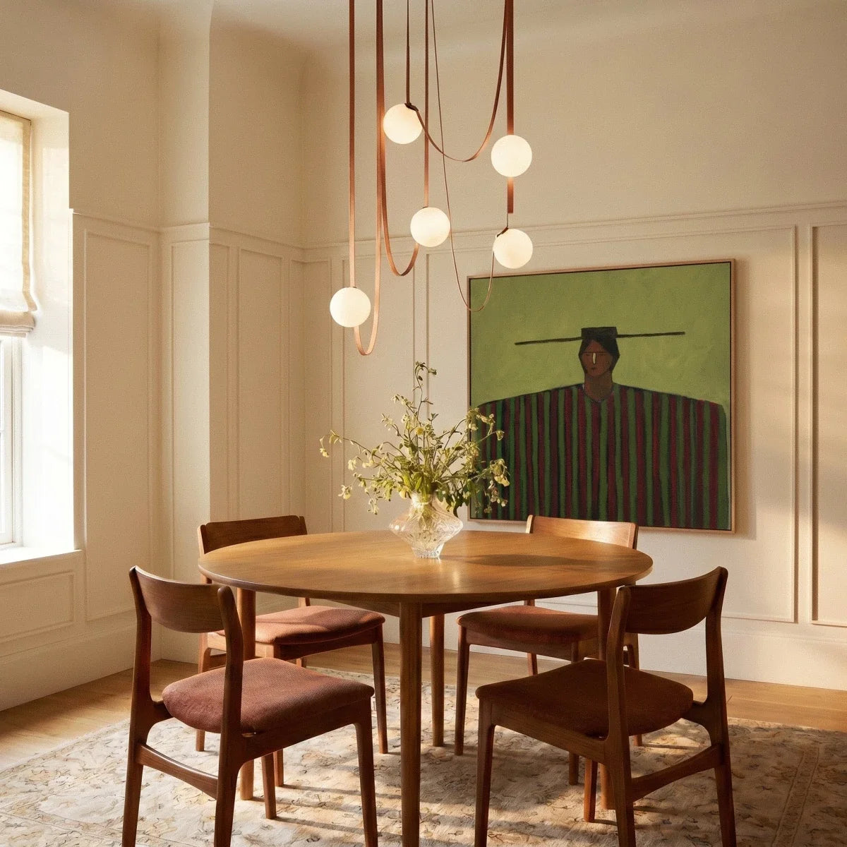 A lit Clérachic chandelier with five glass globes cascades on leather straps above a round wood dining table.