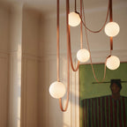 Close-up of a lit Clérachic chandelier's five frosted glass globes on looping leather straps above a dining table.
