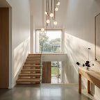 A lit Clérachic chandelier with seven glass globes cascades down a bright stairwell on tan leather straps.