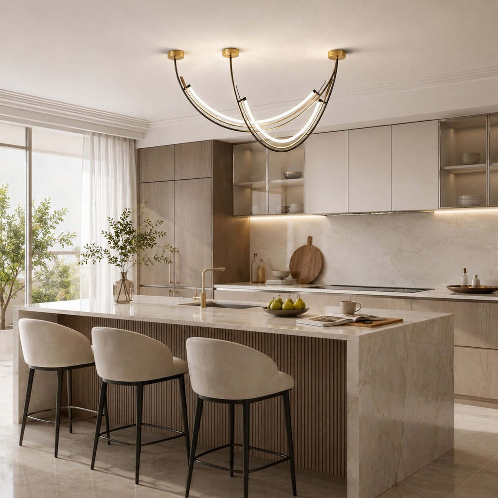 Three brass canopies and curved black arcs, a Clérachic pendant above a stone kitchen island with fluted panels and cream stools.