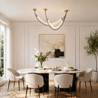 Clérachic arc pendant lit above a round dining table in a white panelled room, with an olive tree and a large abstract print.