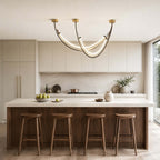Lit Clérachic arc pendant above a kitchen island with four wooden stools, with cream cabinets and a marble splashback behind.