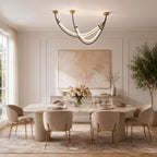 Glowing arc pendant from Clérachic above a long marble dining table and cream chairs with brass legs, with a pink abstract print behind.