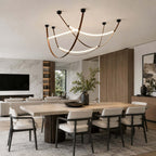 A black-capped Clérachic three-loop pendant set above a pale oak dining table, with a marble feature wall behind.