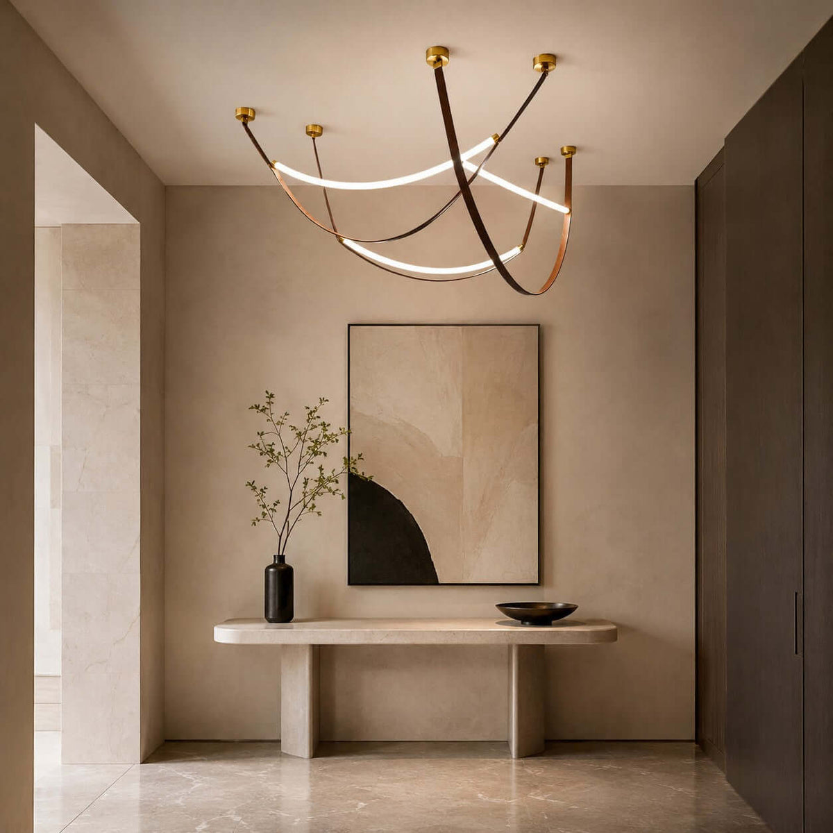 In a hallway, a Clérachic three-loop pendant in gold and brown hangs above a stone console and a large abstract painting.