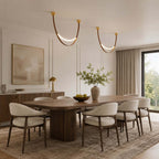 A pair of gold-capped Clérachic loop pendants hang in curves above a long oval dining table with cream armchairs.