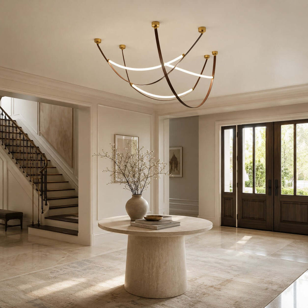 A Clérachic three-loop pendant in gold and brown hangs in a stair hall above a round stone table with a dried-branch vase.
