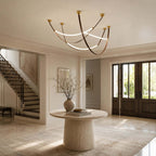 A Clérachic three-loop pendant in gold and brown hangs in a stair hall above a round stone table with a dried-branch vase.