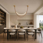 One Clérachic leather loop pendant, lit, hangs above a dining table in a bright room with a kitchen behind.
