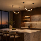 Two black-capped Clérachic leather loops glowing over a marble kitchen island, with a dusk skyline beyond the window.