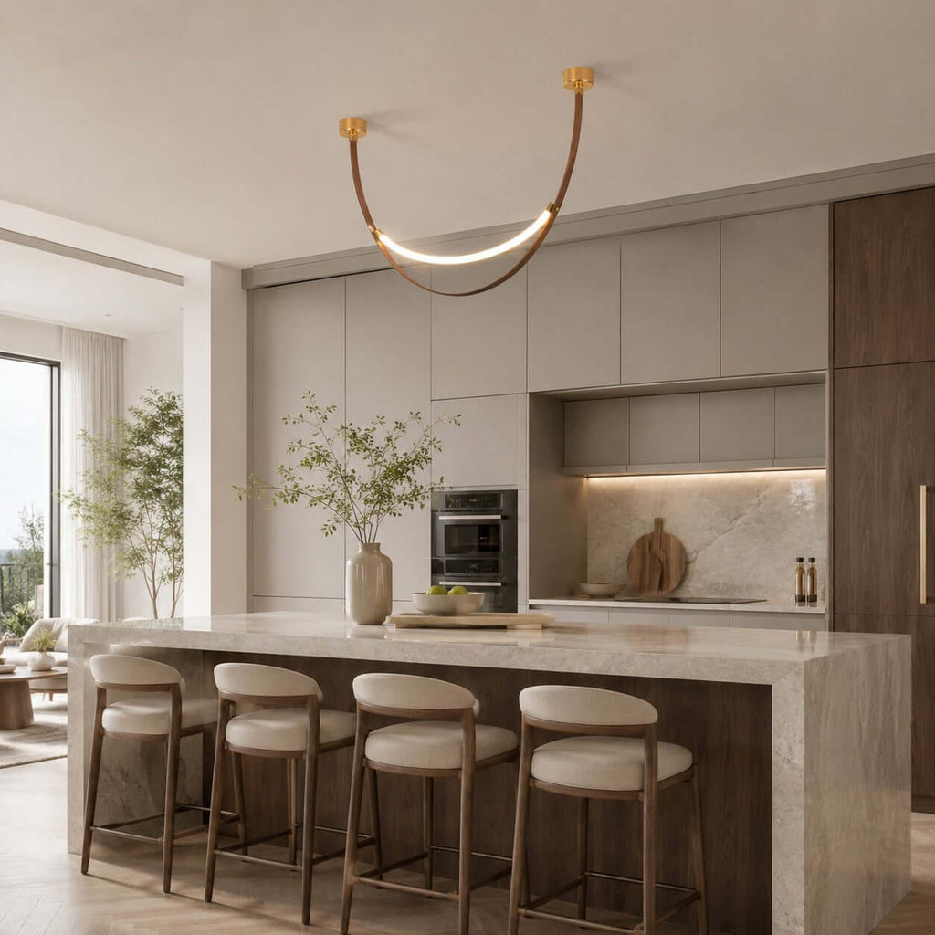 A gold-capped Clérachic loop pendant glows over a marble kitchen island with four cream stools, built-in ovens behind.