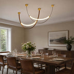 Gold-capped Clérachic loop pendants, a three-piece set, crossing above a laid dining table with a flower arrangement.