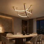 A lit Clérachic three-loop pendant set in gold and brown above a round dining table, with a night-time city view outside.
