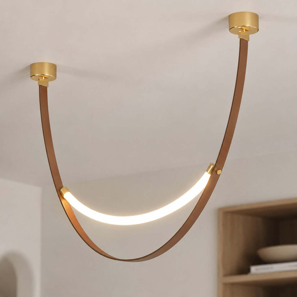 Close view of a gold-capped Clérachic leather loop pendant, its brown strap curving down to a glowing LED strip.
