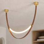 Close view of a gold-capped Clérachic leather loop pendant, its brown strap curving down to a glowing LED strip.