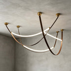 Gold-capped Clérachic three-loop pendant set seen against a concrete ceiling, with lit LED strips and crossing brown straps.