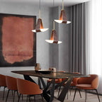 Three Clérachic Leather Pendant Lights glow over a veined stone table with terracotta dining chairs.