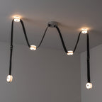 The 6-head Clérachic Leather Strap Chandelier in black leather, zig-zagging across a pale ceiling with nickel fittings.