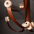 Detail of the Clérachic Leather Strap Chandelier, saddle-leather straps looped tight around glowing alabaster disc heads.
