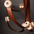 Detail of the Clérachic Leather Strap Chandelier, saddle-leather straps looped tight around glowing alabaster disc heads.