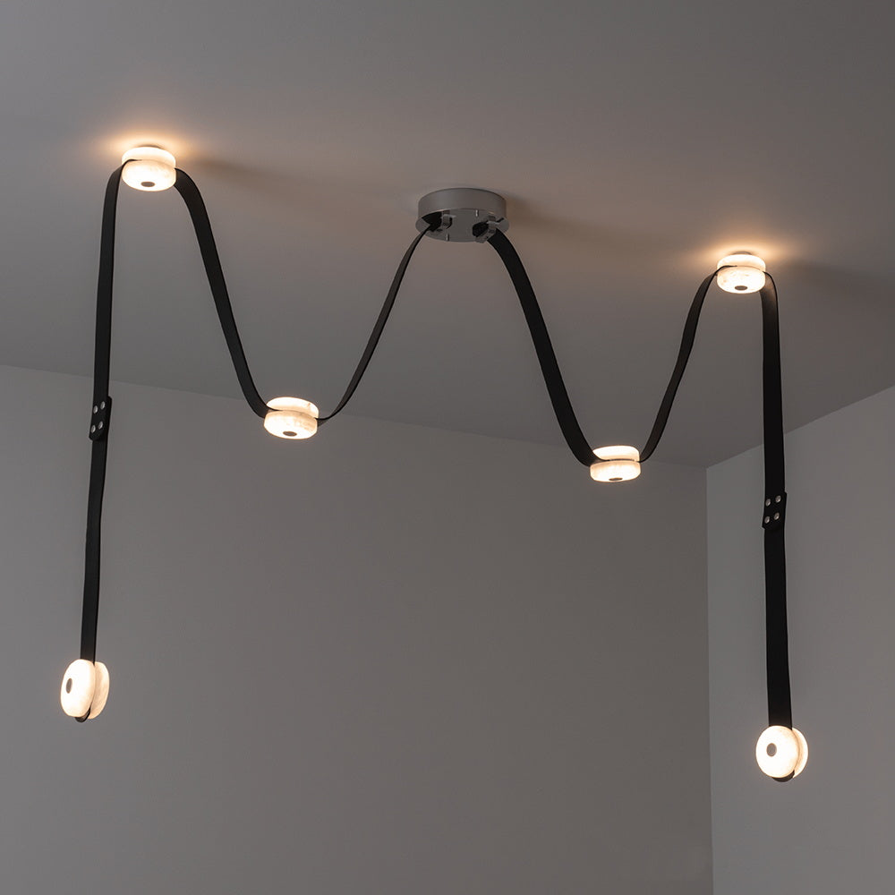 Black leather Clérachic Leather Strap Chandelier lit above a corner, six alabaster discs spaced along the strap run.