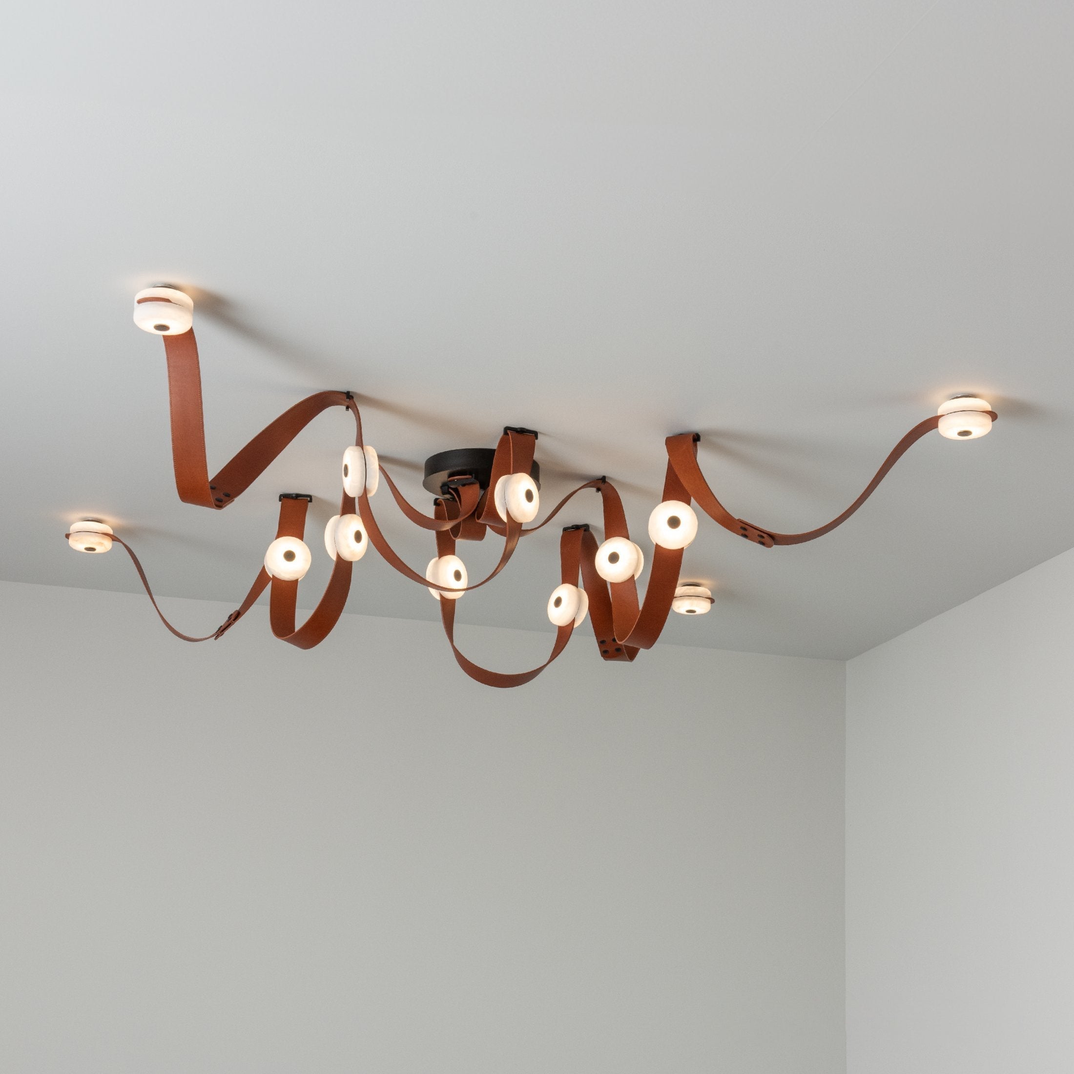 Cognac leather and black fittings on the Clérachic Leather Strap Chandelier, twelve alabaster discs lit across the ceiling.