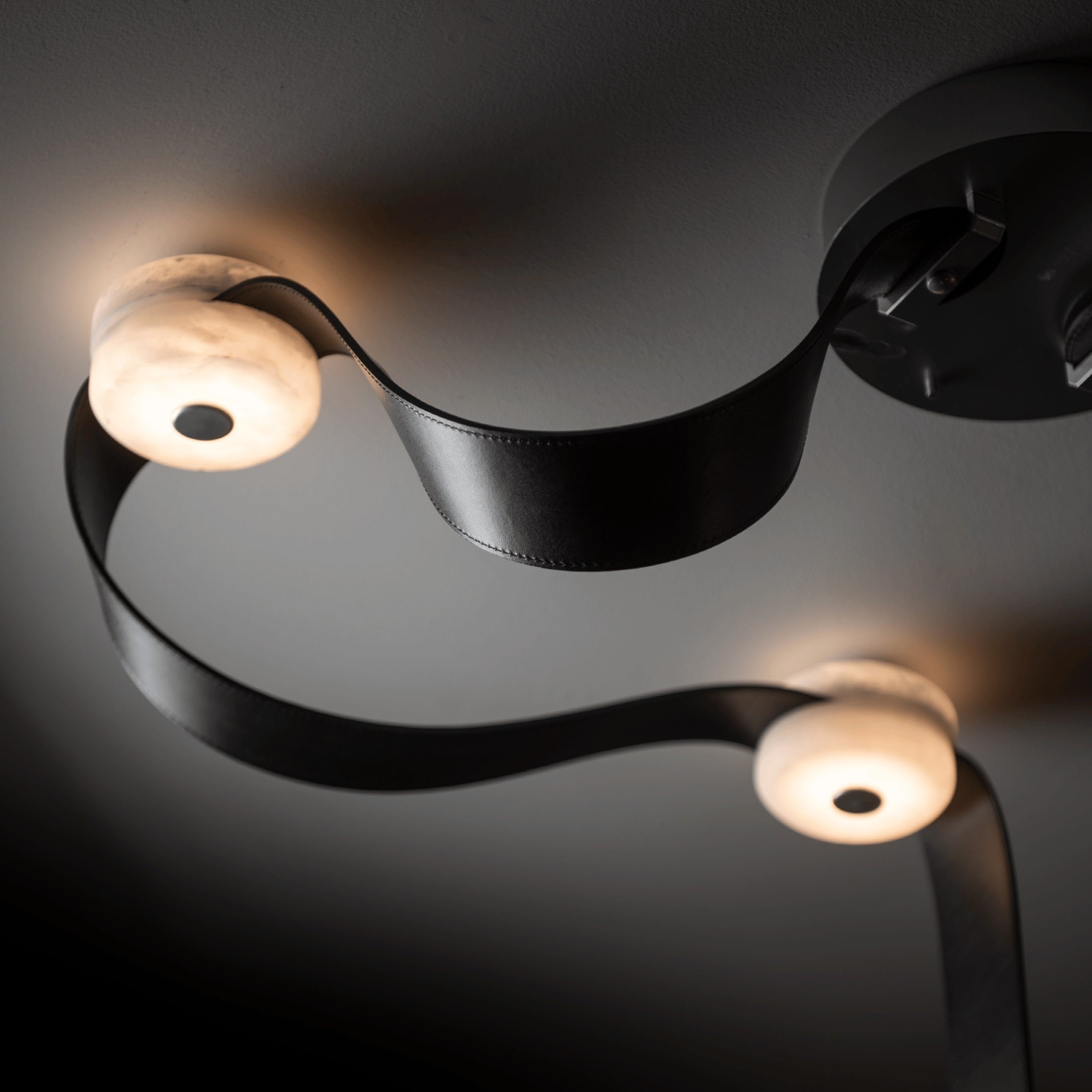 Black saddle leather curving away from the ceiling canopy on the Clérachic Leather Strap Chandelier, alabaster discs aglow.