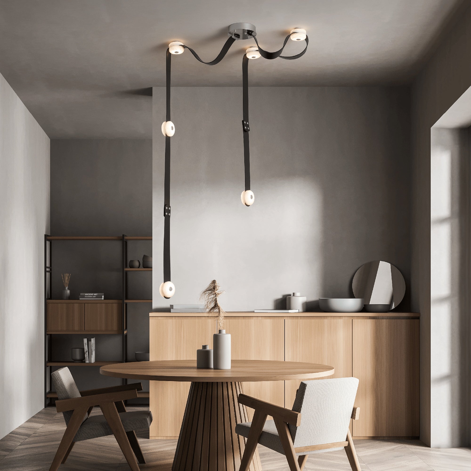 Black straps of the Clérachic Leather Strap Chandelier trailing down beside an oak sideboard over a round dining table.