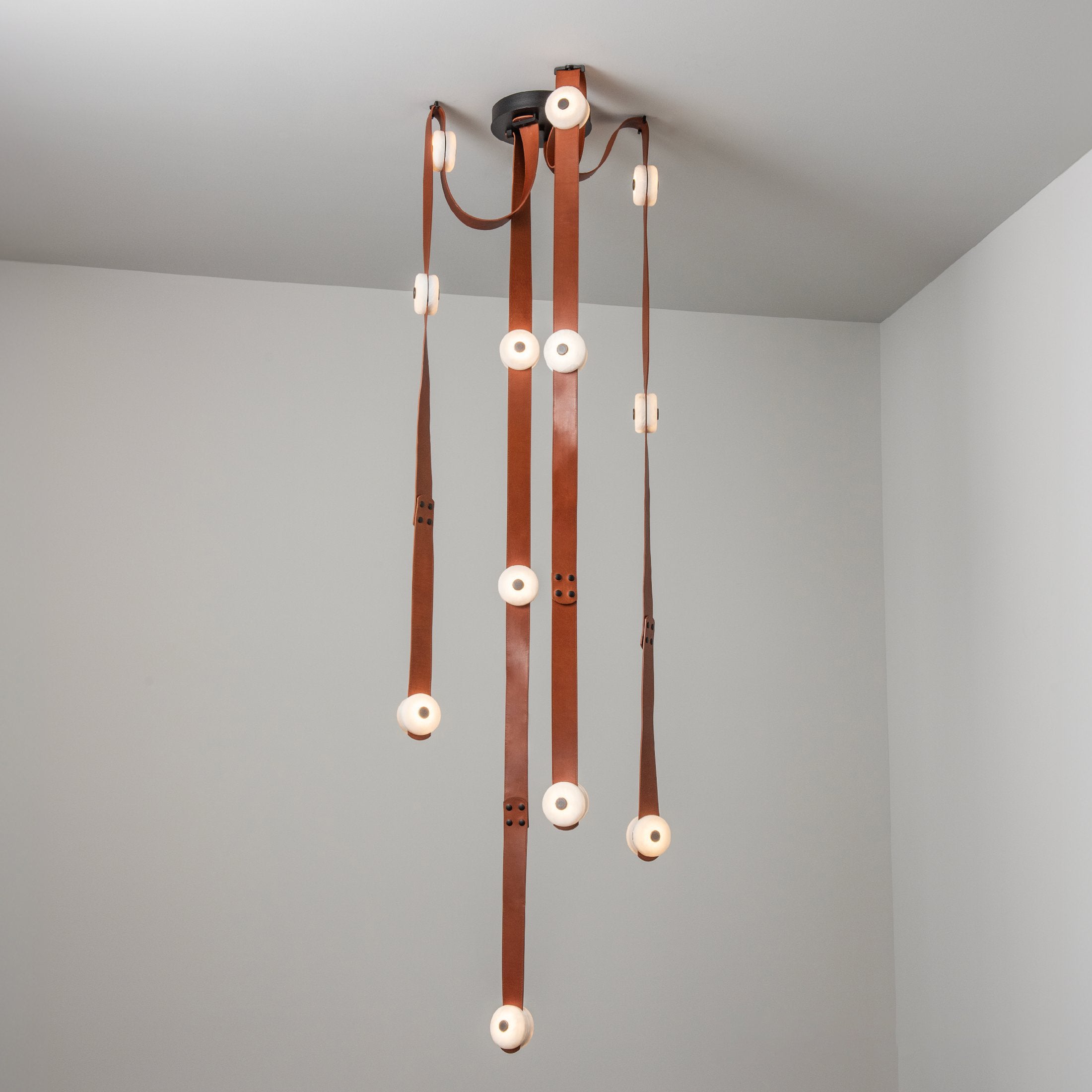 Long cognac straps of the Clérachic Leather Strap Chandelier falling far below the ceiling, sized for a stairwell.