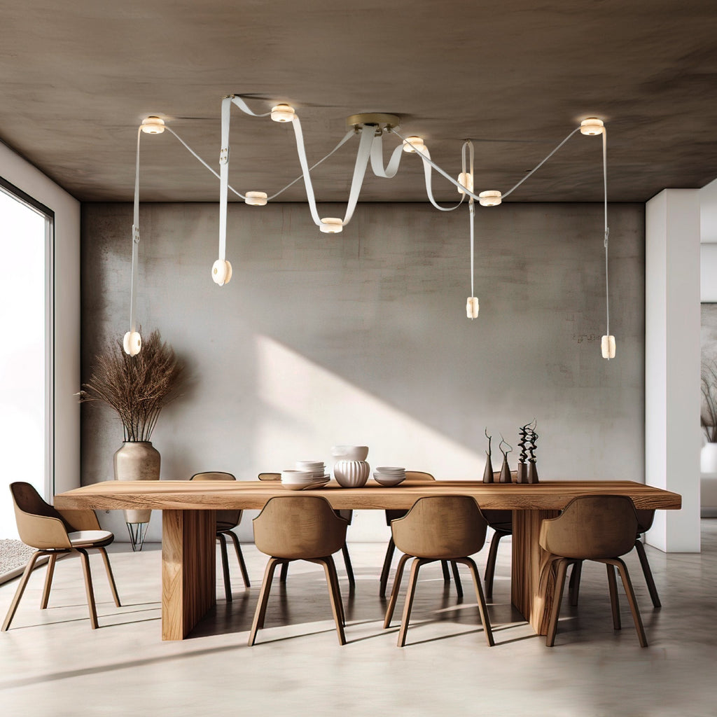 White Clérachic Leather Strap Chandelier stretched over a long oak dining table against a concrete wall.