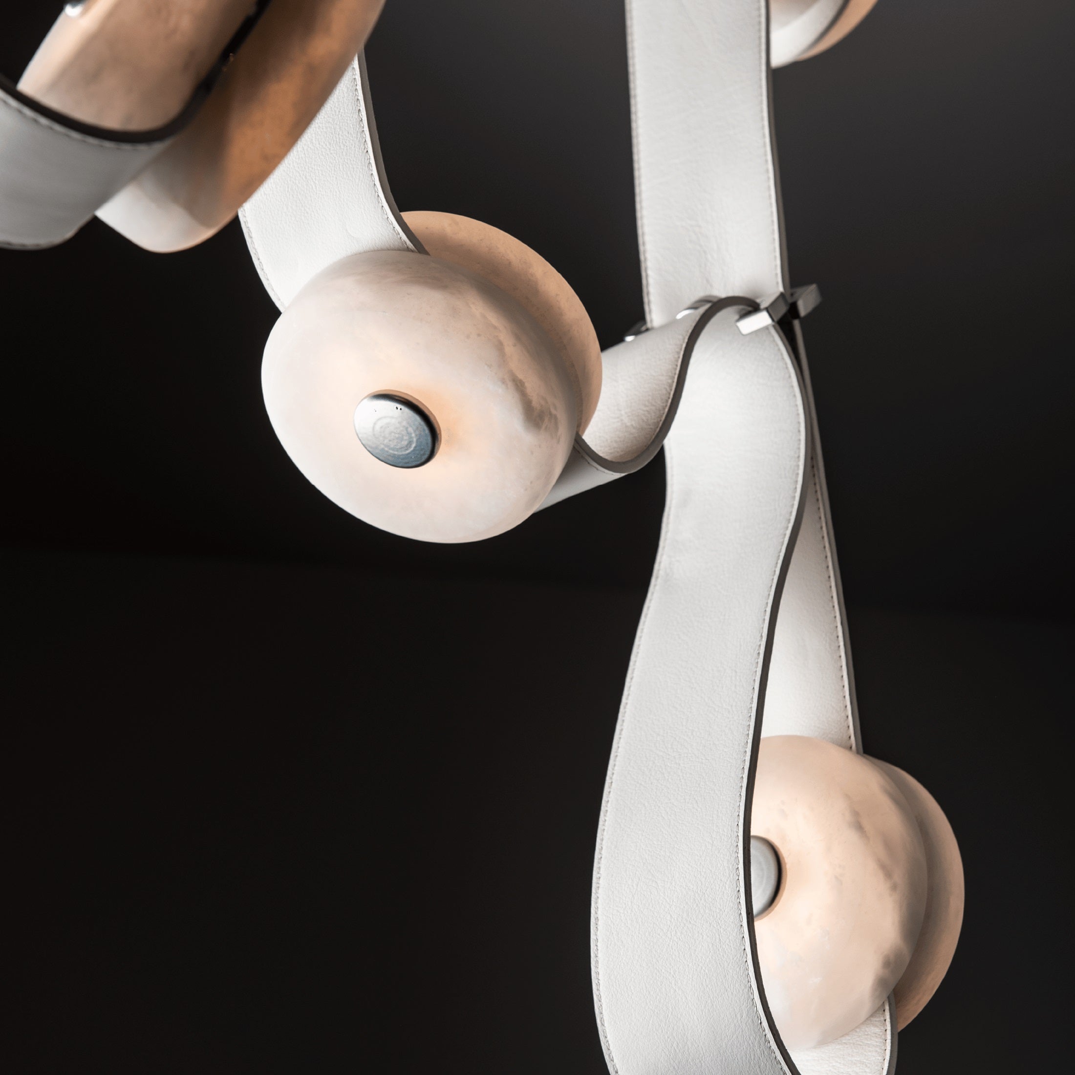 White leather straps and alabaster discs on the Clérachic Leather Strap Chandelier, shot against a black background.