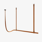 Tan leather strap light on a plain white backdrop, with two straps dropping from the ceiling and a long strap curving into a horizontal bar, from Clérachic.