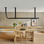 Black leather strap pendant carrying a long light bar above a pale wood dining table, a wooden bench and a framed print, from Clérachic.
