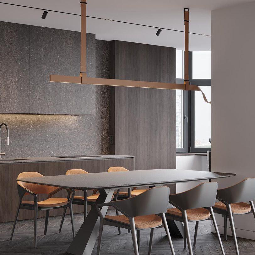 Tan strap pendant with a horizontal light bar above a dark dining table and leather-seat chairs in a dark-panelled kitchen, from Clérachic.