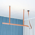 Tan leather straps and a slim light bar hang below a ceiling canopy, with blue and white curtains behind, from Clérachic.